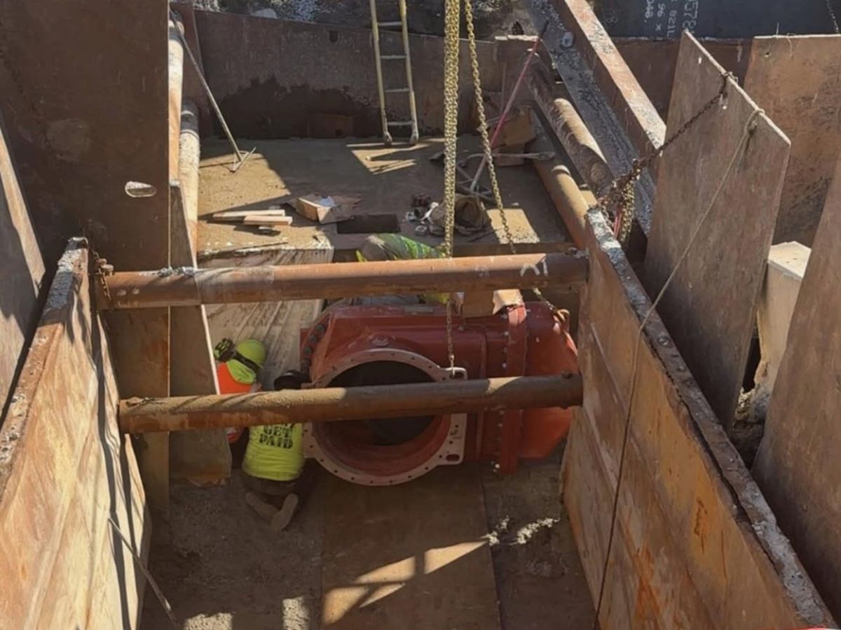 Two JLA & Sons crew members setting a large red 36-inch butterfly valve at the bottom of a braced, shored excavation.