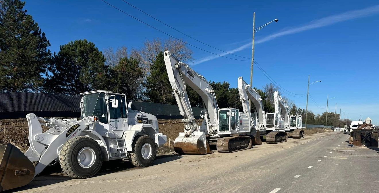 A white JLA & Sons wheel loader and four white excavators lined up along a roadway on the I-294 job.