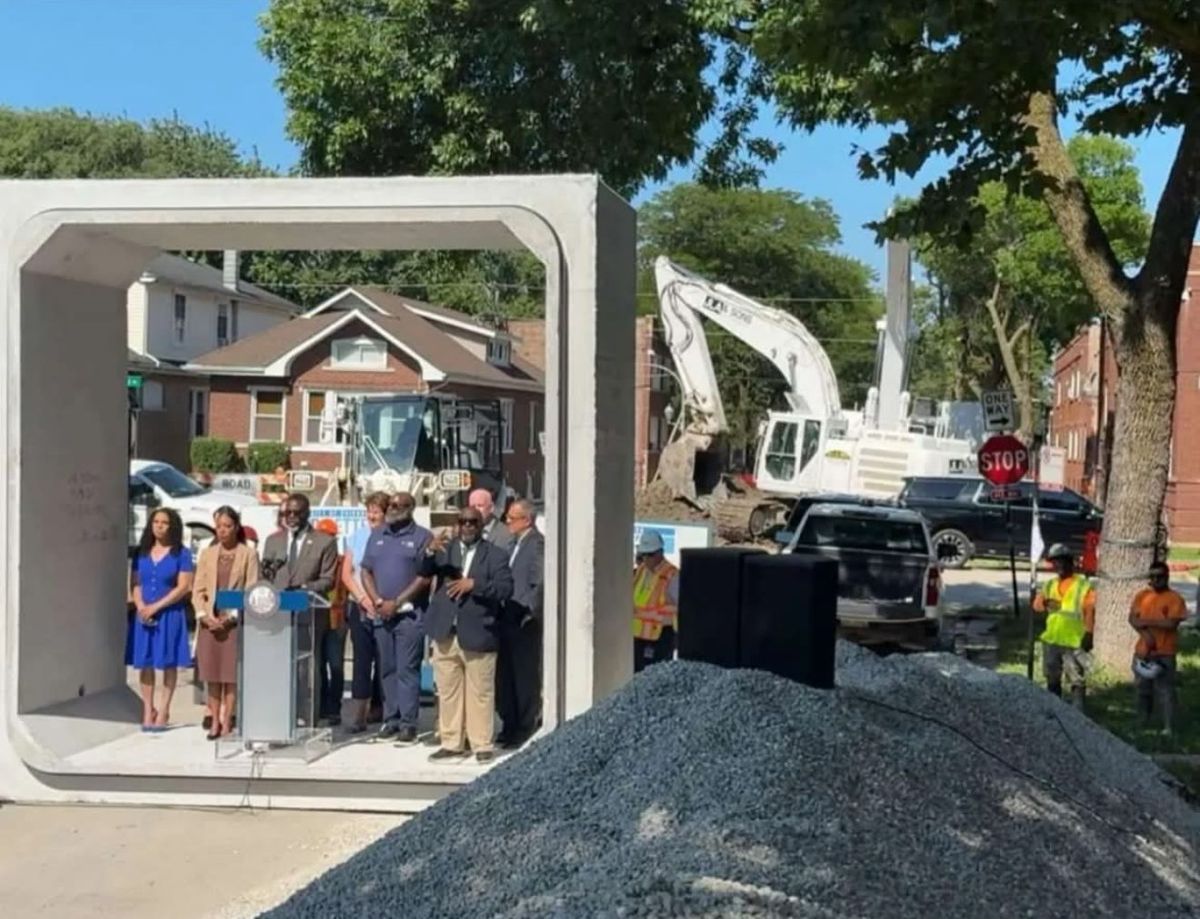 City of Chicago officials holding a press event inside a precast box culvert section at the Le Moyne and Luna job site, with a JLA & Sons excavator in the background.